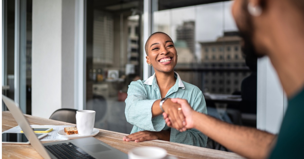 Photo showing a woman making an introduction and shaking hands with someone across a table.