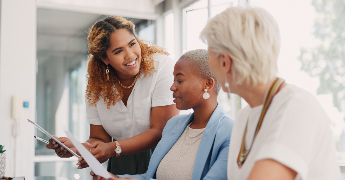 Photo of three women talking at work, discussing recent organizational changes, which were surely made even better by the use of AI.