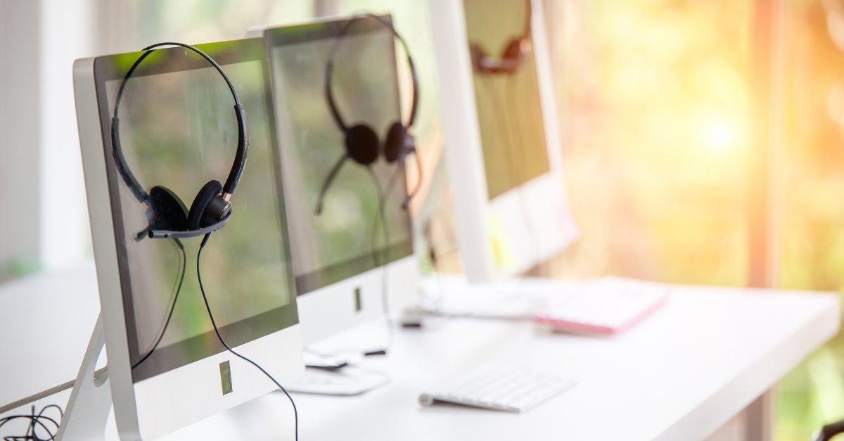 Photo of headsets hanging on computer monitors in a contact center, representing virtual agent trends.