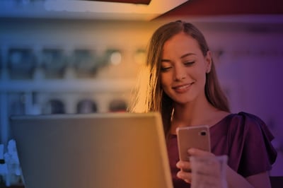 Woman smiling using phone and laptop.